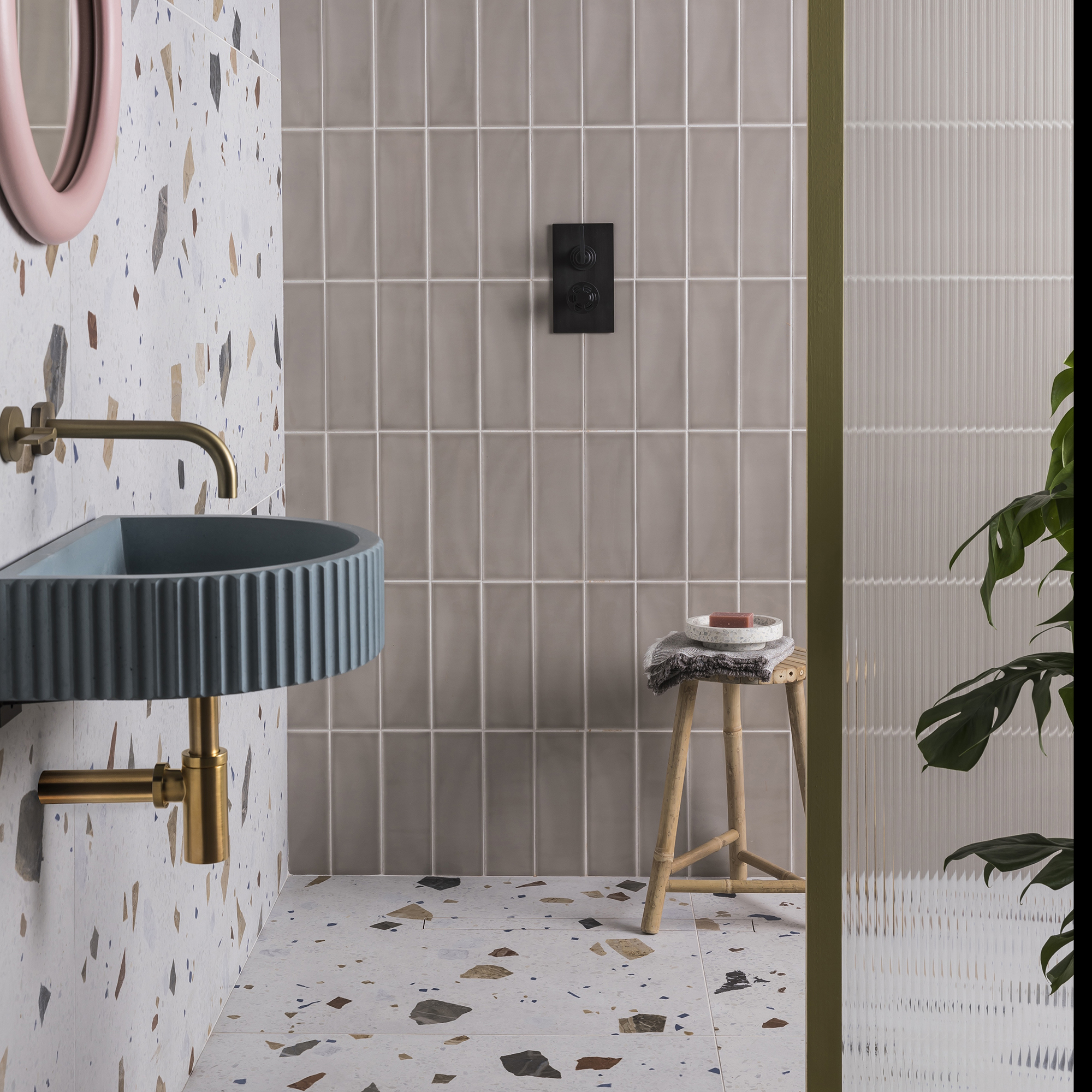 Baño moderno con lavabo flotante acanalado, grifo mezclador dorado en la pared, espejo rosa, azulejos grises en la pared y baldosas de terrazo en el suelo