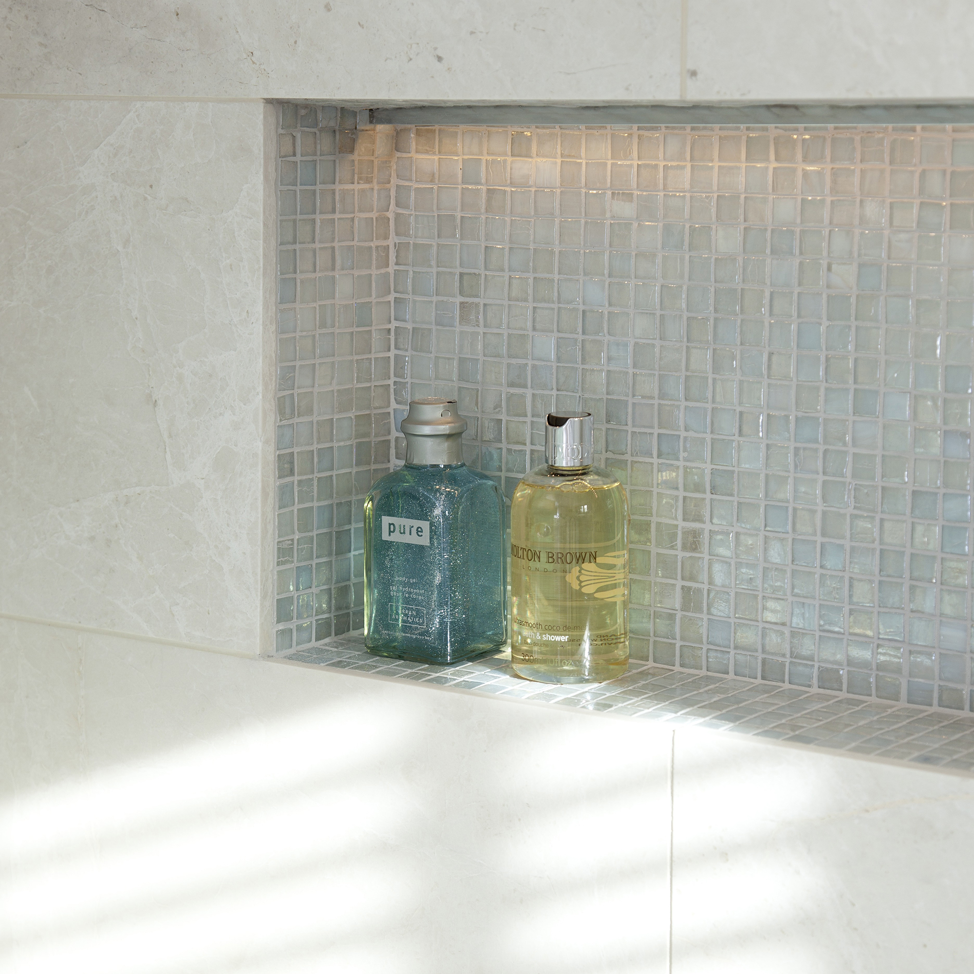 iluminacion para ducha: nicho de baño de mosaico con iluminación empotrada y botellas de artículos de tocador.