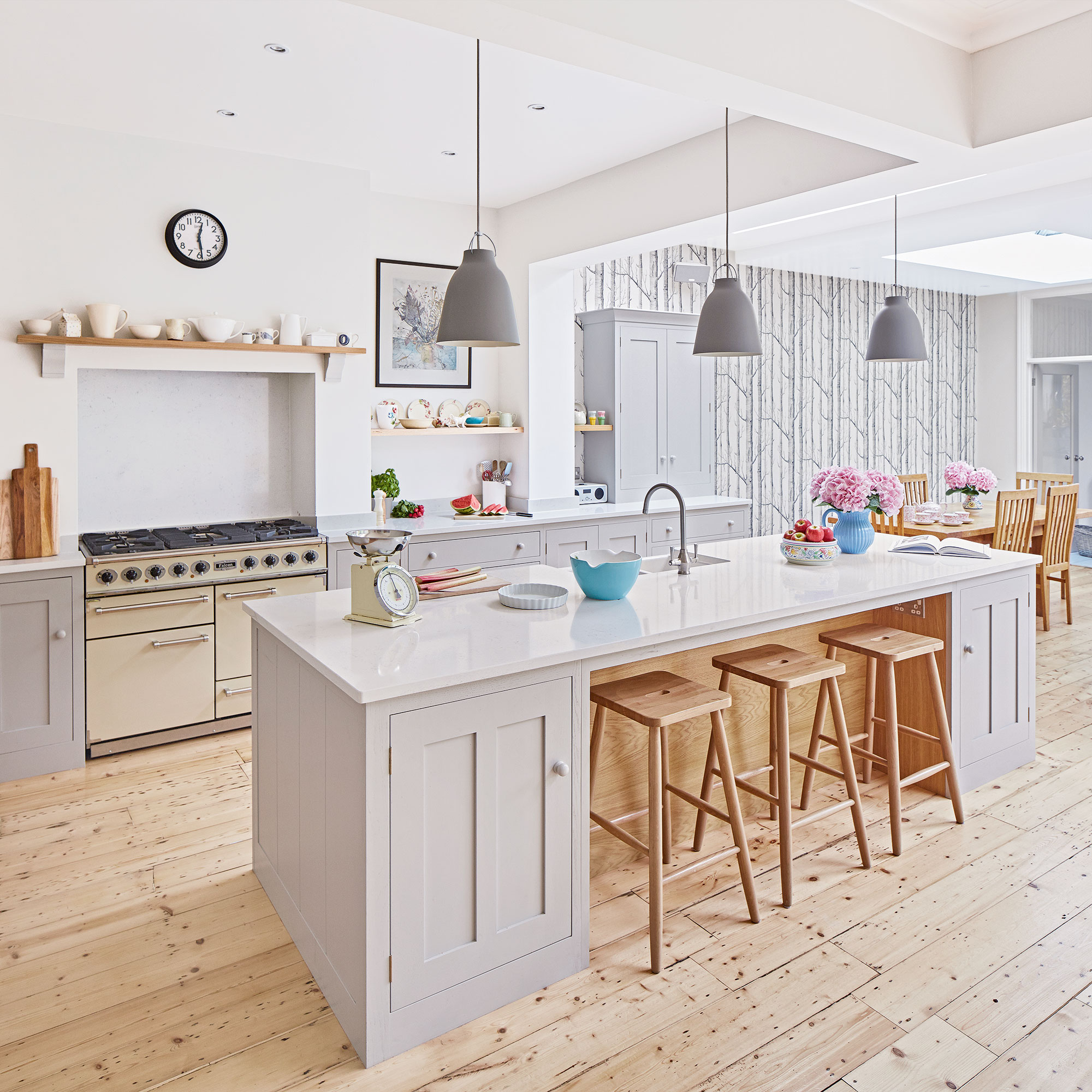 Cocina neutral con estufa, isla con asientos, lámparas colgantes y piso de madera